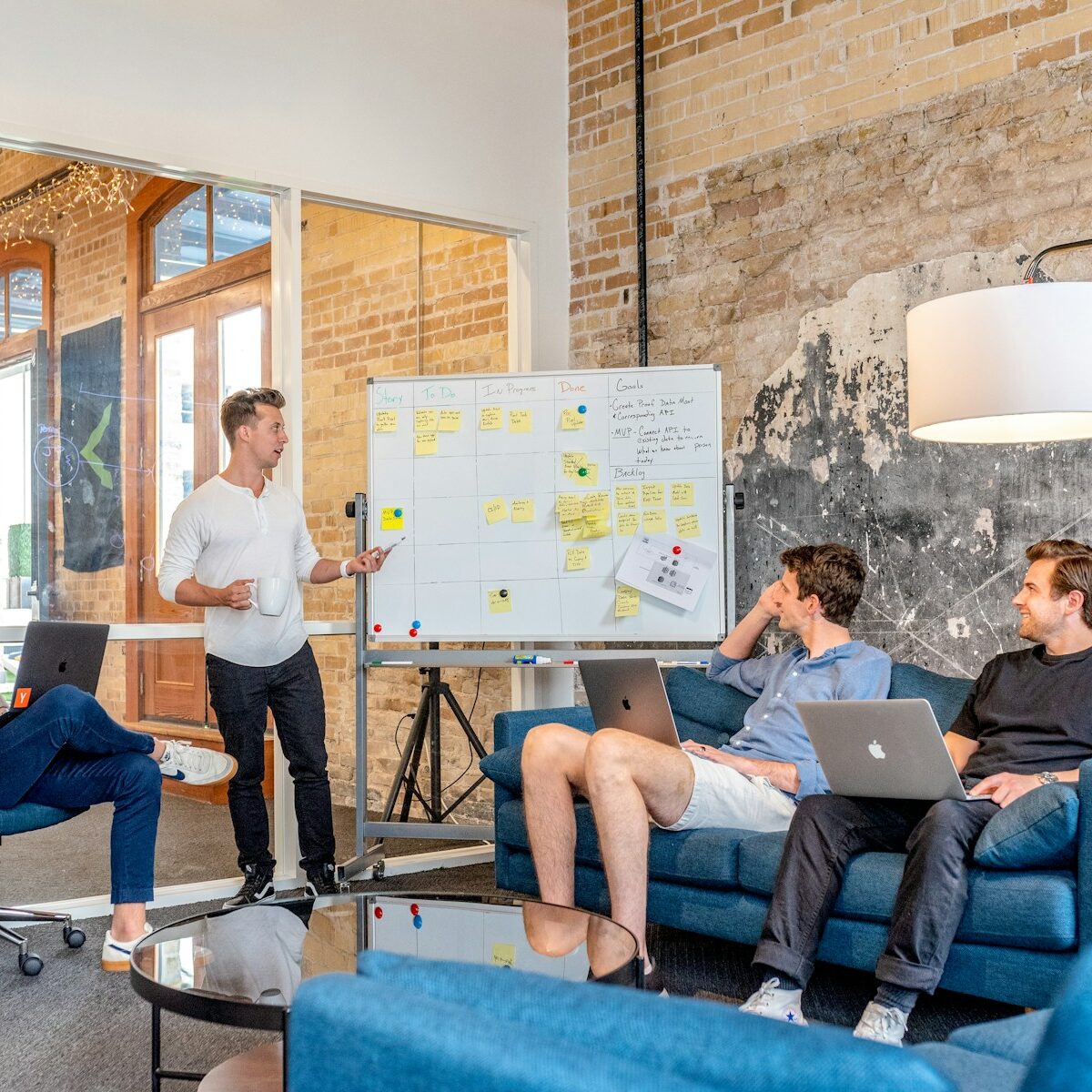 three men sitting while using laptops and watching man beside whiteboard